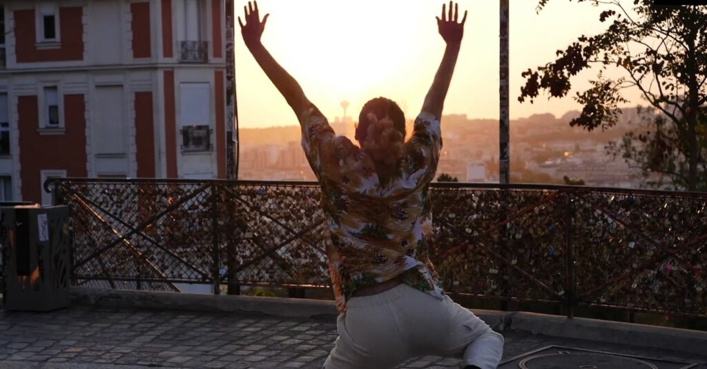 Un jeune homme (Max), dansant de dos devant un coucher de soleil.